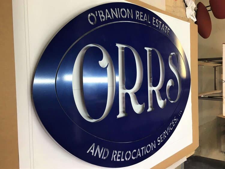 O'Banion Real Estate and Relocation Services oval sign in navy with cutout lettering.