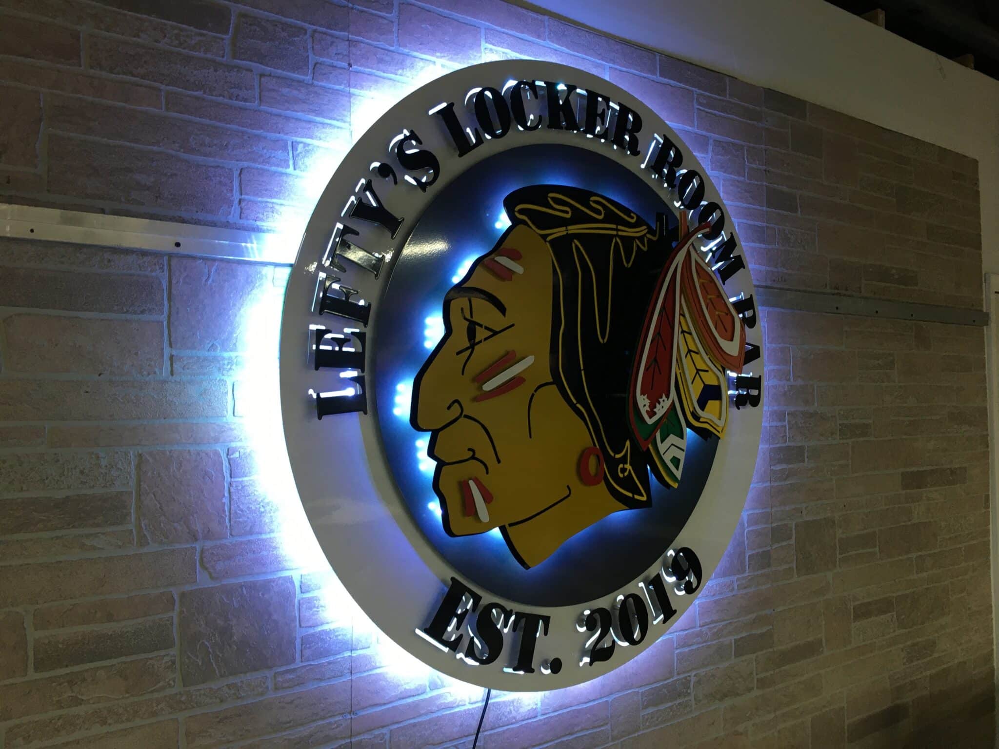Backlit metal bar sign installed indoors with warm halo glow against textured wall