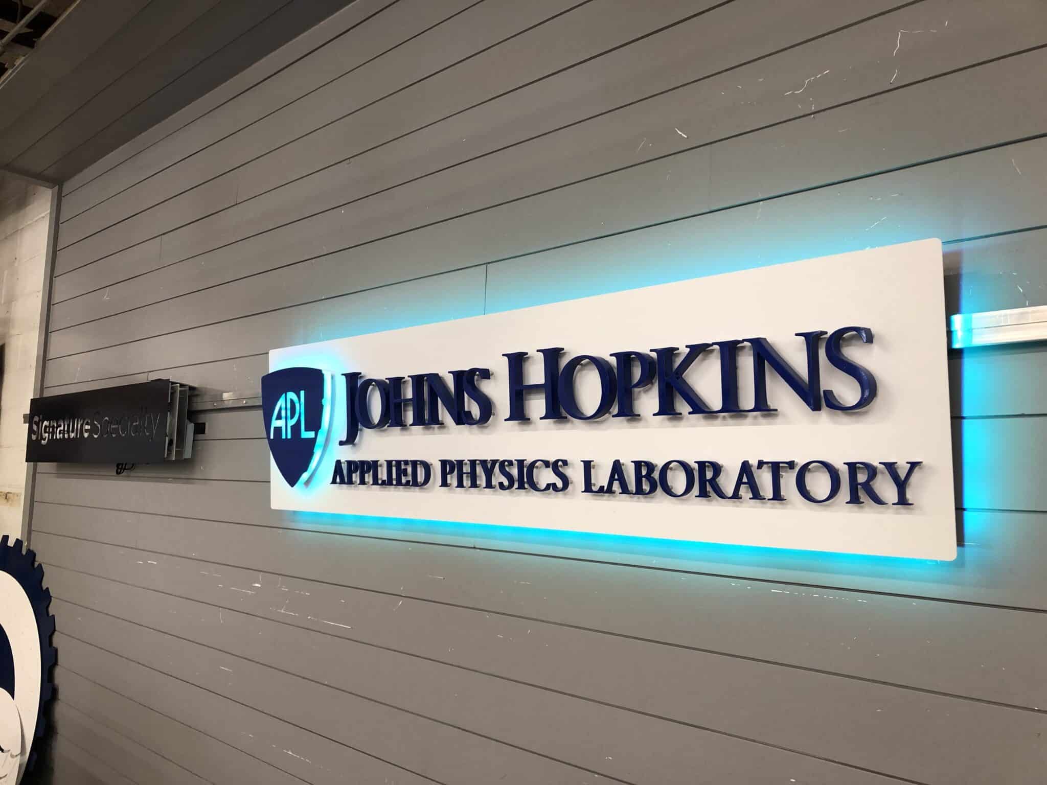 Brushed metal halo-lit institutional logo sign mounted in a lobby