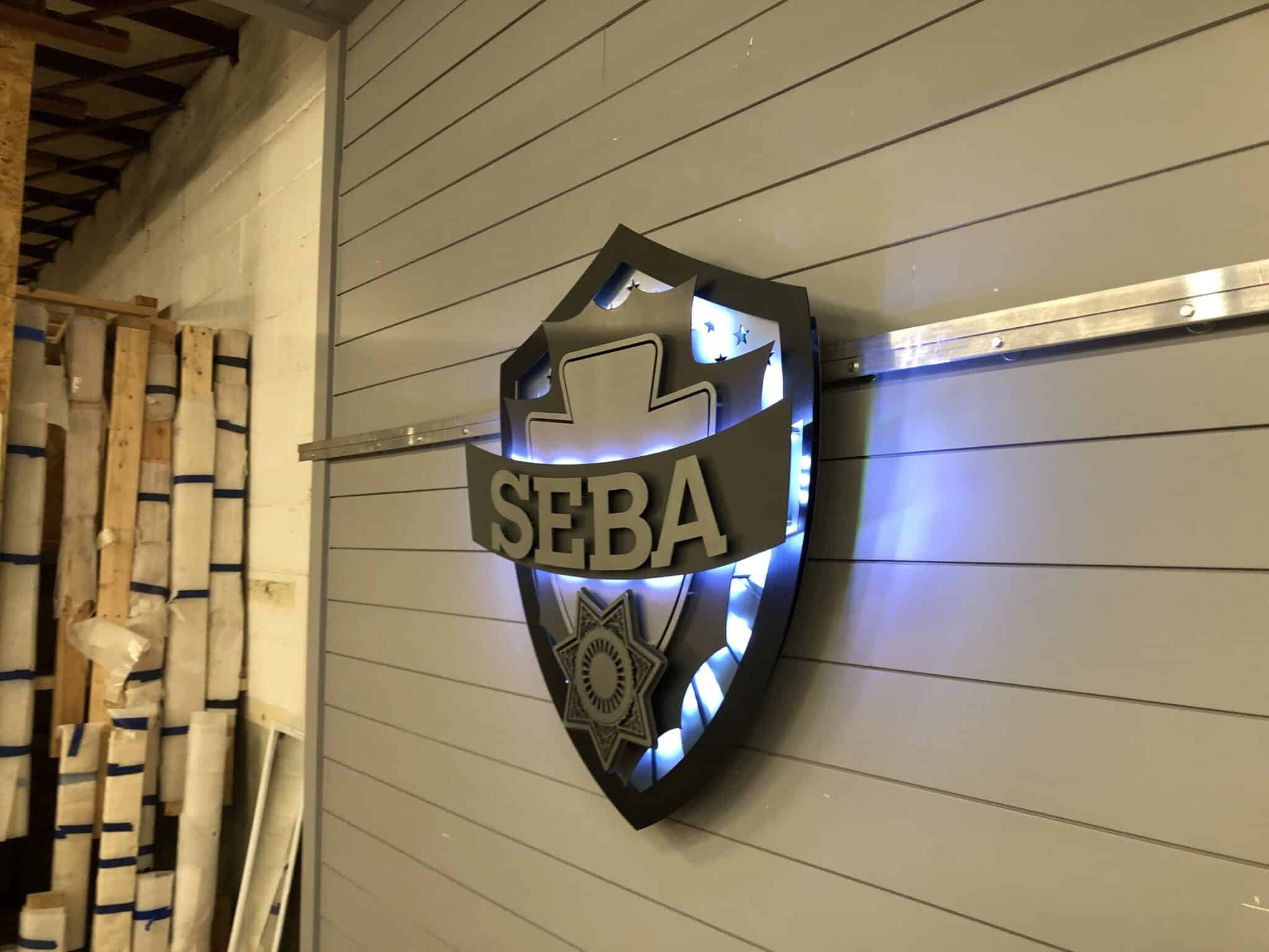 Halo-lit metal company logo sign with a soft glow on an office wall