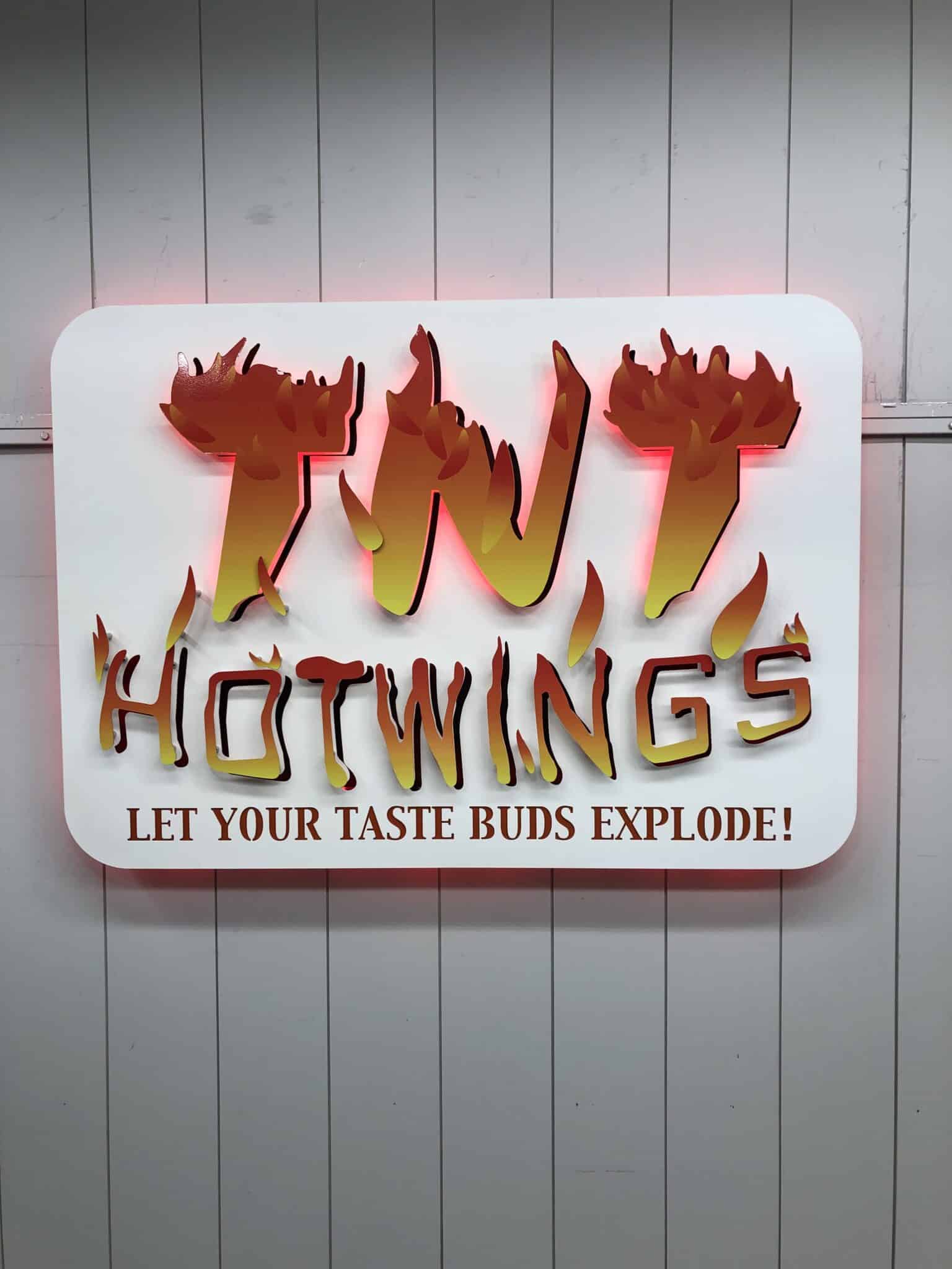 Backlit metal custom restaurant sign for TNT Hot Wings mounted on storefront exterior