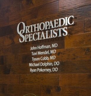 Orthopaedic Specialists dimensional letters on a dark wood wall, the physicians' names listed beneath.