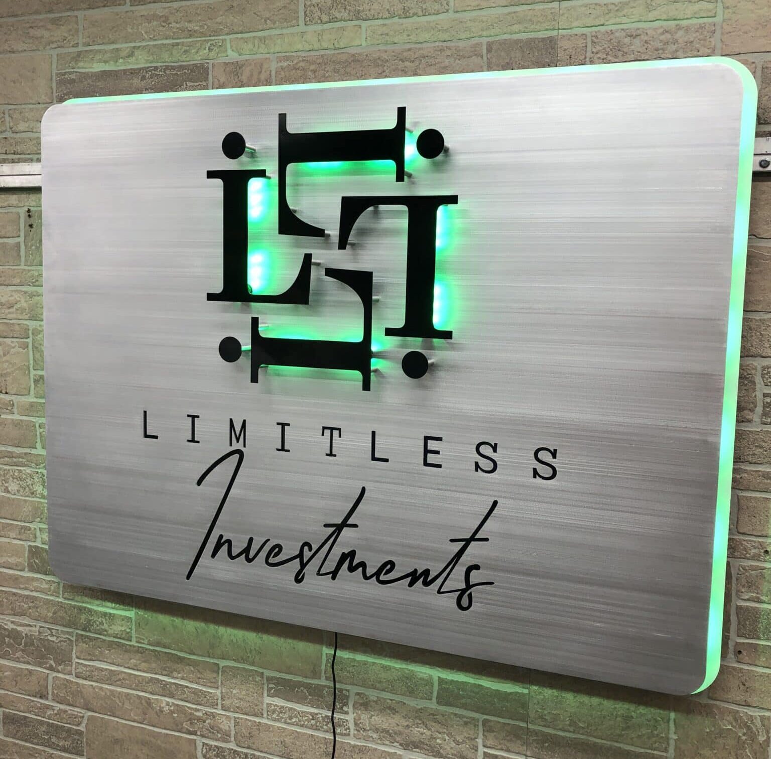 Limitless Investments brushed aluminum panel sign with a black LI monogram, halo-lit LED and glowing green.