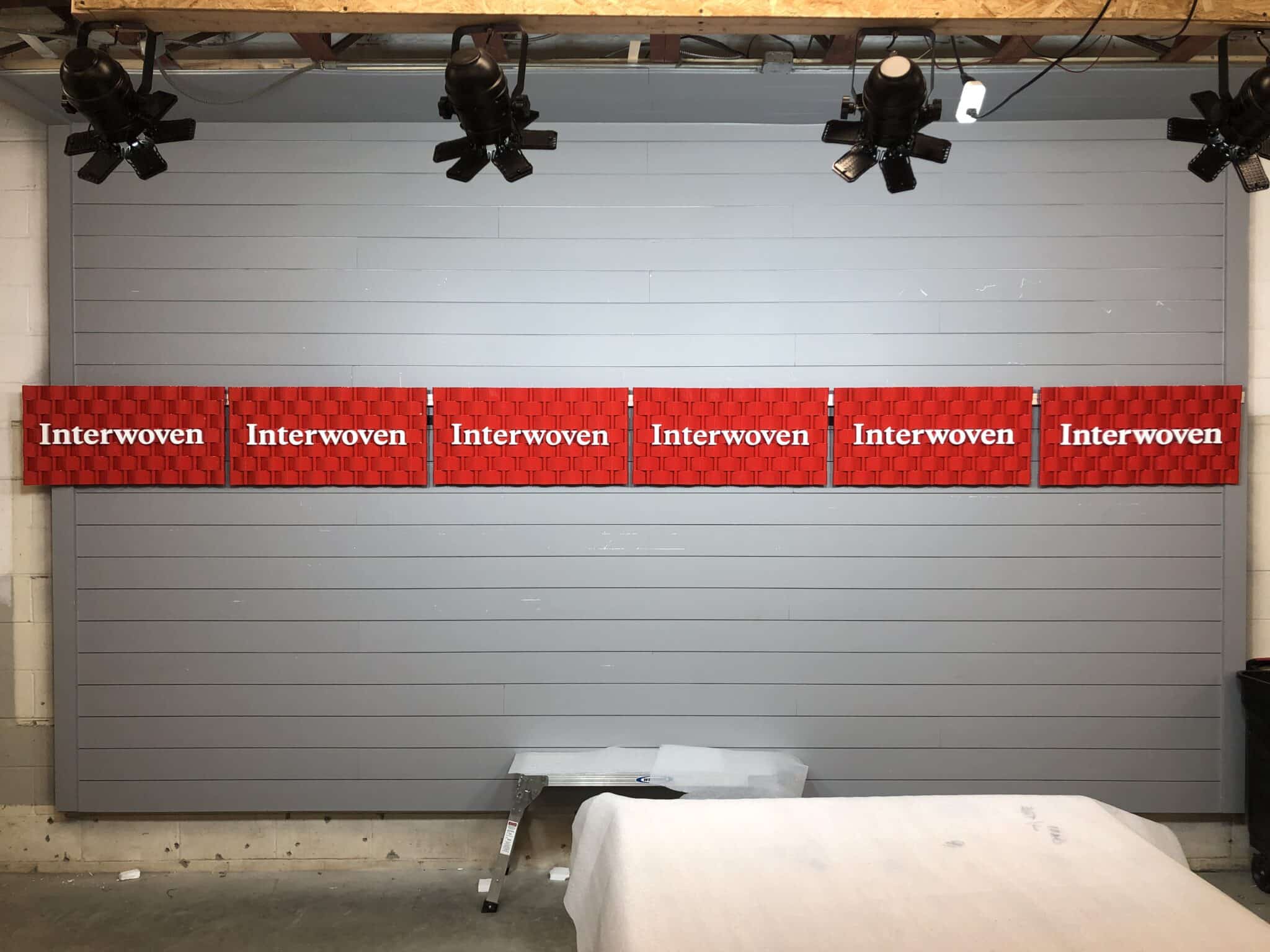 Six finished Interwoven woven metal signs spotlit and lined up after fabrication