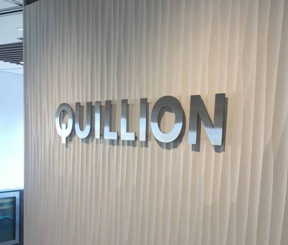 Quillion dimensional letters in polished aluminum, mounted on a fluted white wall.