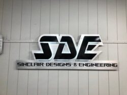 Sinclair Designs & Engineering sign with a black and white SDE monogram above the full name.