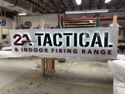 2A Tactical and Indoor Firing Range panel sign in black and red on white, photographed in the shop before installation.