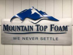 Mountain Top Foam sign with a navy mountain range above the name and the line We Never Settle.