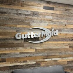 GutterMaid dimensional letters in brushed aluminum with a swoosh underline, mounted on a reclaimed wood wall.