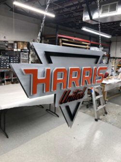 Harris United shield sign hanging from a chain in the shop, red lettering on brushed aluminum.