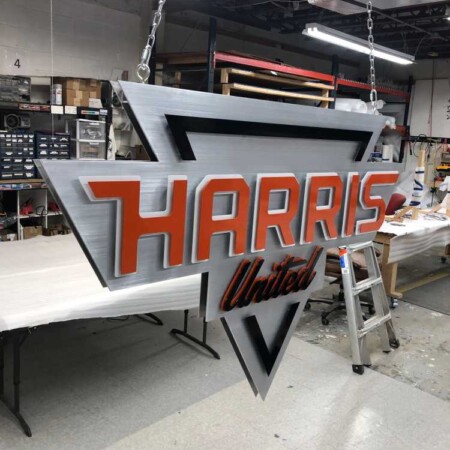 Harris United shield sign hanging from a chain in the shop, red lettering on brushed aluminum.
