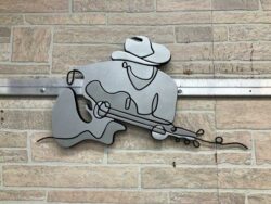 Cut-out steel wall art of a cowboy playing guitar, mounted on stone veneer.