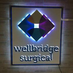 Wellbridge Surgical sign with a four-petal diamond above the name, halo-lit LED and glowing blue.