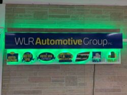 WLR Automotive Group sign with a row of service brand panels beneath the name, glowing green.