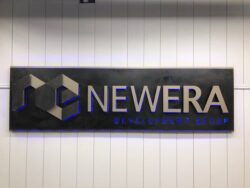 NEWERA Development Group sign in blued steel with gold lettering and a cube mark, glowing softly from behind.