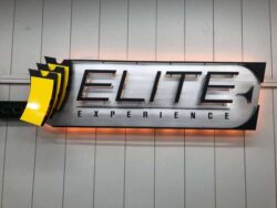 Elite Experience sign with a gold ticket beside brushed lettering, halo-lit LED and glowing warm.