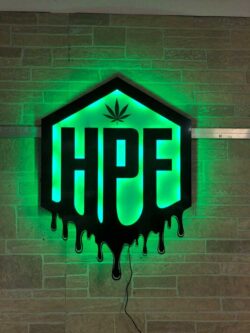 Hunny Pot Farms hexagon sign from a slight angle, the green LED halo flooding the brick behind it.