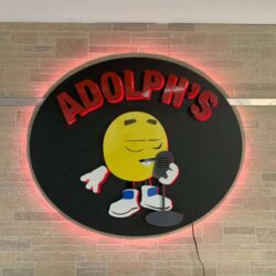 Adolph's round sign on stone, the cartoon lemon at the microphone with a red LED halo behind.