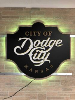 City of Dodge City, Kansas sign in black with gold script lettering, glowing warm yellow on brick.