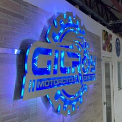 Gilroy Motorcycle Center sign from an angle, blue light spilling through the gear teeth onto the wall.