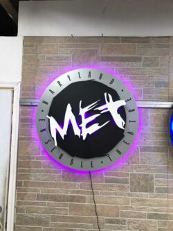 The Maryland Ensemble Theater sign on the brick wall, its purple halo spreading across the courses.