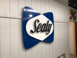 Sealy logo sign in navy and white, the script set in a white lens across a navy diamond.