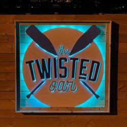 The Twisted Oar sign with crossed oars over a teal and orange disc, framed in timber.