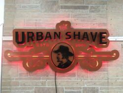The Urban Shave sign with a barber portrait between scrollwork, glowing warm amber on stone.