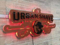 The Urban Shave sign with the halo switched to red, the scrollwork reading in silhouette.