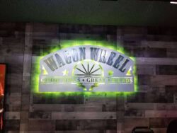 Wagon Wheel sign on a plank wall, Good Times Great Friends beneath the arch, glowing green.