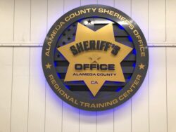 Alameda County Sheriff's Office Regional Training Center seal in gold and navy with a star badge at its center, backed by a blue LED glow.