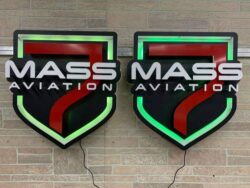 Two Mass Aviation shield signs side by side, halo-lit green, mounted on stone.