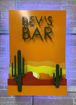 Bev's Bar panel sign angled on the wall, cacti and a layered desert sunset below the cut name.