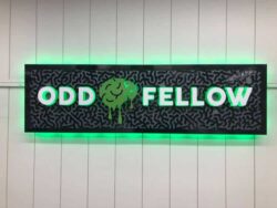Odd Fellow sign in textured black with a green brain between the words, halo-lit LED and glowing green.