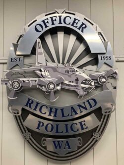 Richland Police badge sign unlit, showing the layered steel patrol car and aircraft detail above the name banner.