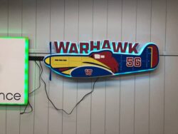 Warhawk sign shaped as a P-40 fighter in blue and red with the number 56 on its tail.