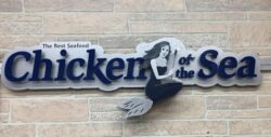 Chicken of the Sea logo sign with the mermaid and blue script lettering, mounted on stone veneer.