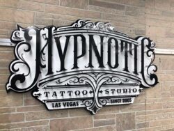 Hypnotic Tattoo Studio sign in ornate black and white lettering with scrollwork, mounted on stone