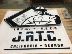 IBEW NECA JATC California Nevada sign laid flat in the shop, a lineman above the lettering.