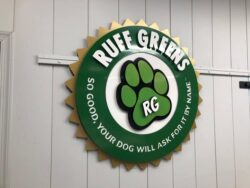 Ruff Greens round sign with a scalloped green edge and a paw print, So Good Your Dog Will Ask For It By Name.