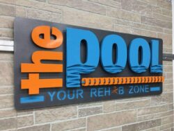The Pool Your Rehab Zone sign, orange and blue letters over a water graphic and a lane rope.