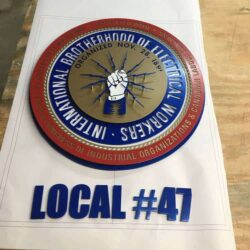 IBEW Local #47 seal laid flat in the shop, a raised fist and lightning inside a red and blue ring.