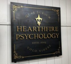 Hearthfire Psychology blued-steel sign in slate and gold with a lantern emblem and Latin mottoes.