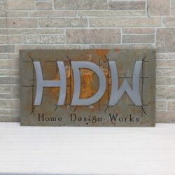 HDW Home Design Works sign, brushed letters on a rusted steel plate with a scored border.