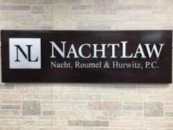 NachtLaw sign on a dark timber plank, an NL monogram beside the firm name.
