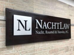 The NachtLaw plank sign from an angle, the raised letters catching light across the grain.