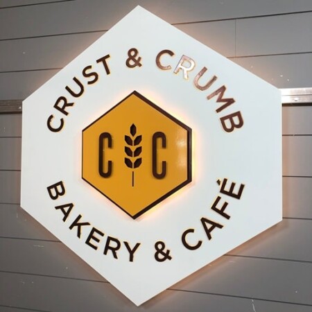 Crust & Crumb Bakery & Café hexagonal sign in white, with a yellow hexagon monogram and a wheat stalk.