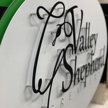 Close view of the Valley Shepherd Creamery script, black letters on standoffs above the white oval.