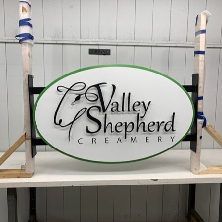 Valley Shepherd Creamery oval sign clamped upright in the shop, green edge around a white face.