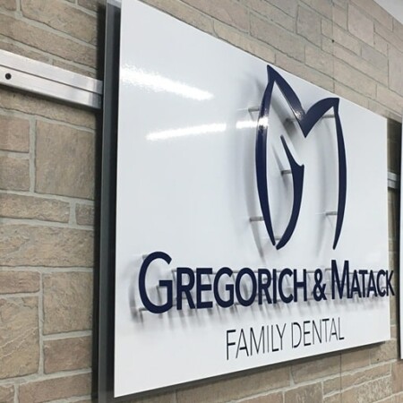 Gregorich & Matack Family Dental sign angled against the stone, the navy letters standing off the white face.